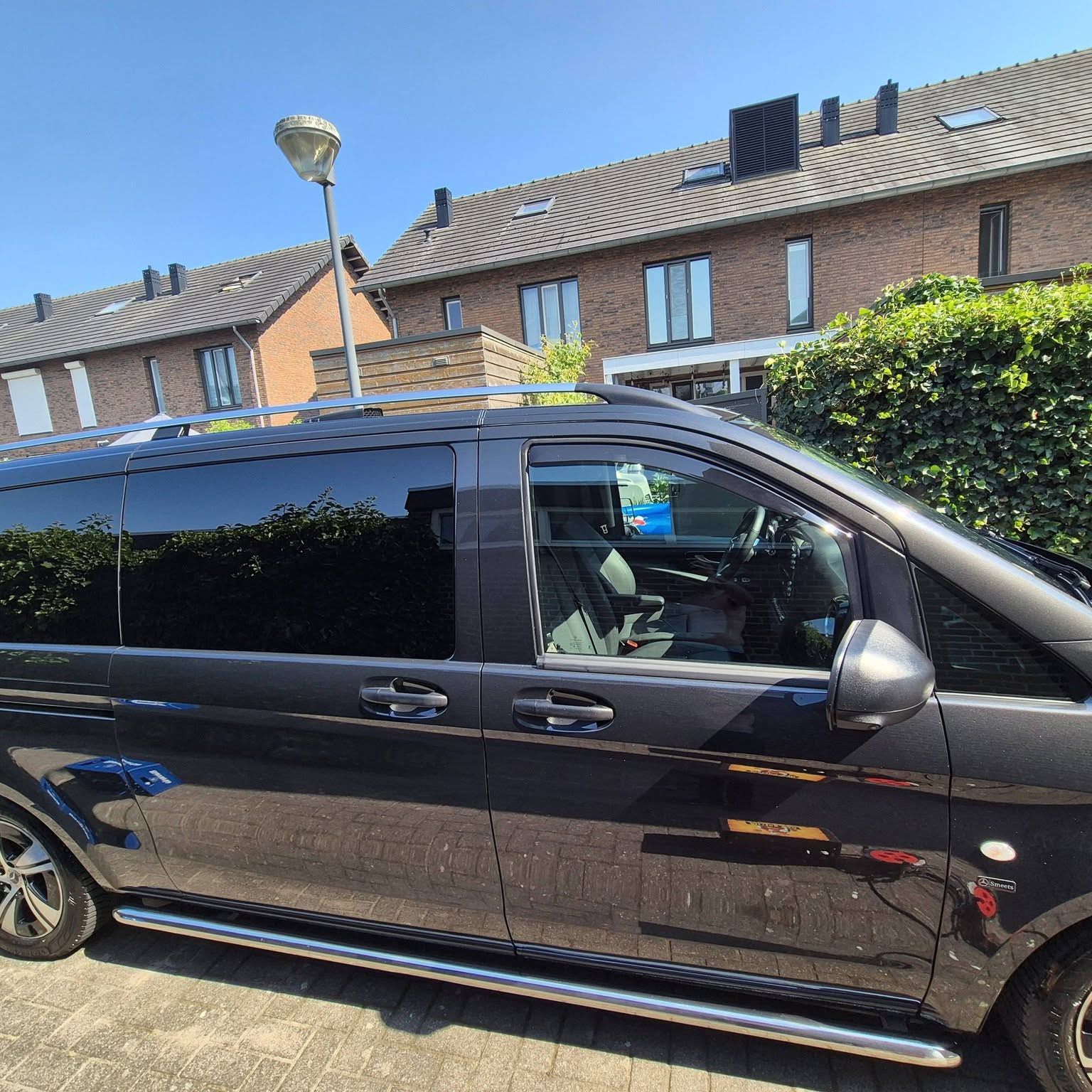 Zwarte Mercedes-Benz bus in de zon, de lak spiegelt de heg